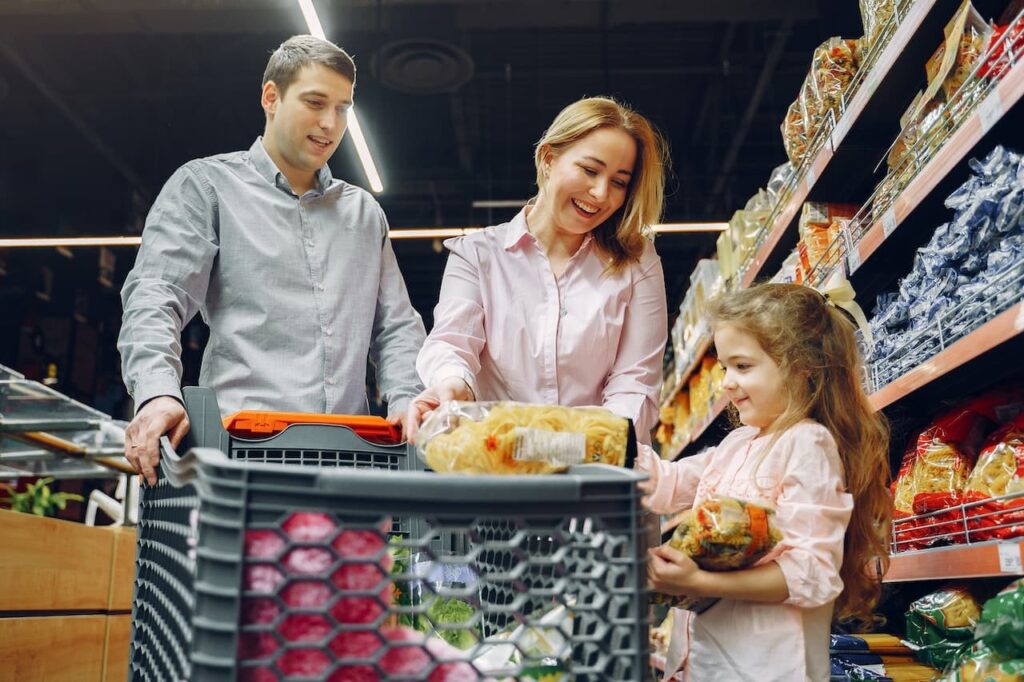 Parents shopping with a kids with a cart full of grocery in front of them